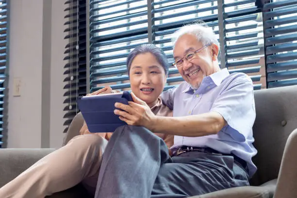 Senior asian couple looking at a tablet and enjoying their newly digitized family photos
