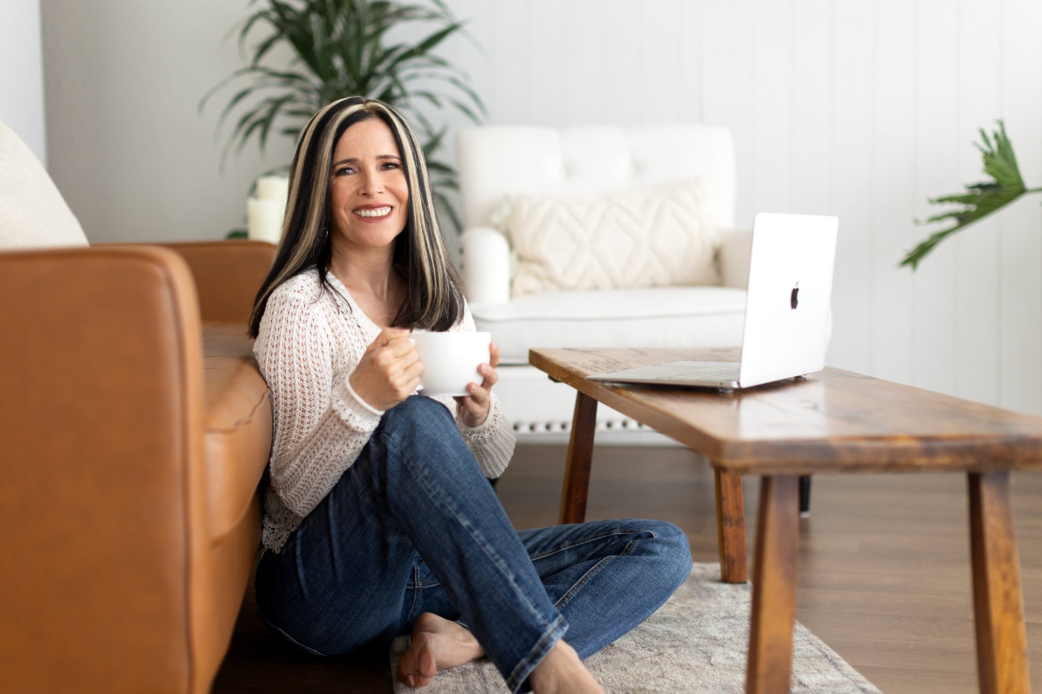 Image of Kathleen Becker, Post Falls Idaho Photo Manager and organizer, sitting on the floor in front of a couch sipping a cup of tea and smiling warmly into the camera